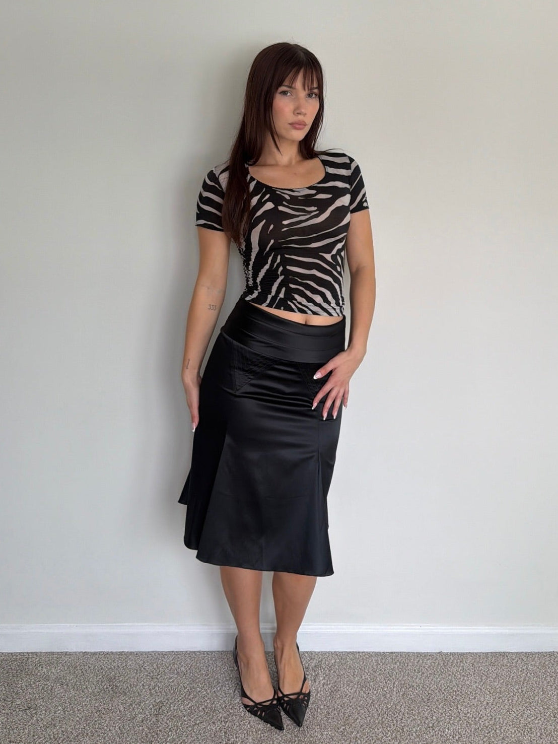 Woman wearing a zebra print top and black skirt against a plain wall.
