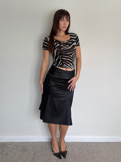 Woman wearing a zebra print top and black skirt against a plain wall.