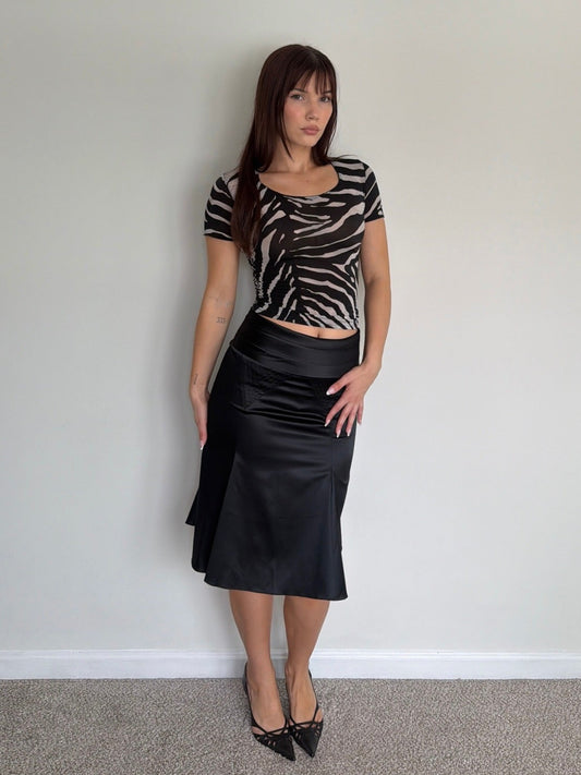 Woman wearing a zebra print top and black skirt against a plain wall.