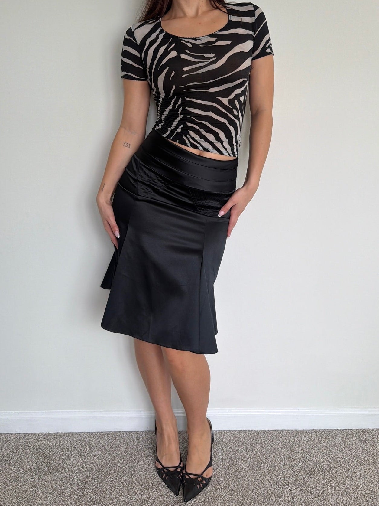 Woman wearing a zebra print top and black skirt against a plain wall.