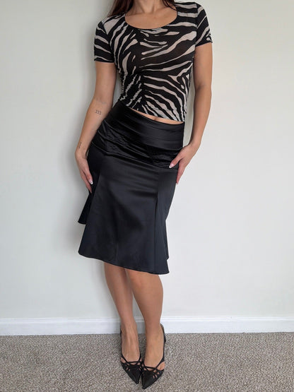 Woman wearing a zebra print top and black skirt against a plain wall.