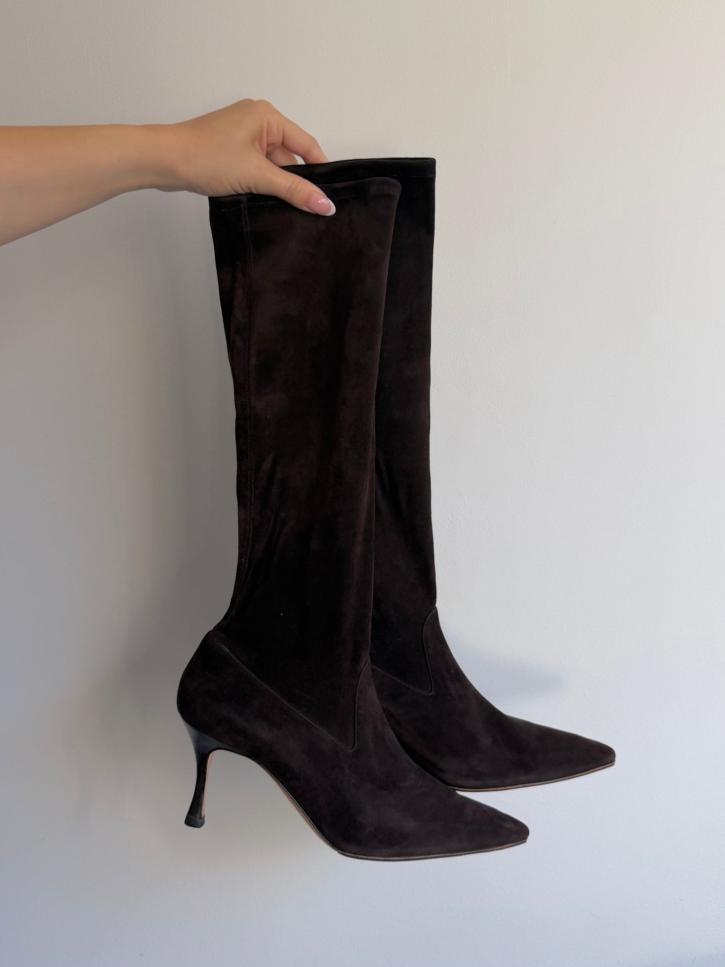 Black knee-high boots being held by a hand on a white background