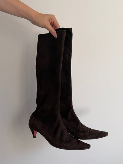 Brown knee-high boots held by a hand against a plain background
