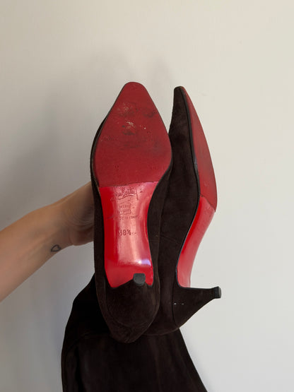 Black high-heeled shoe with a red sole held by a hand against a white background