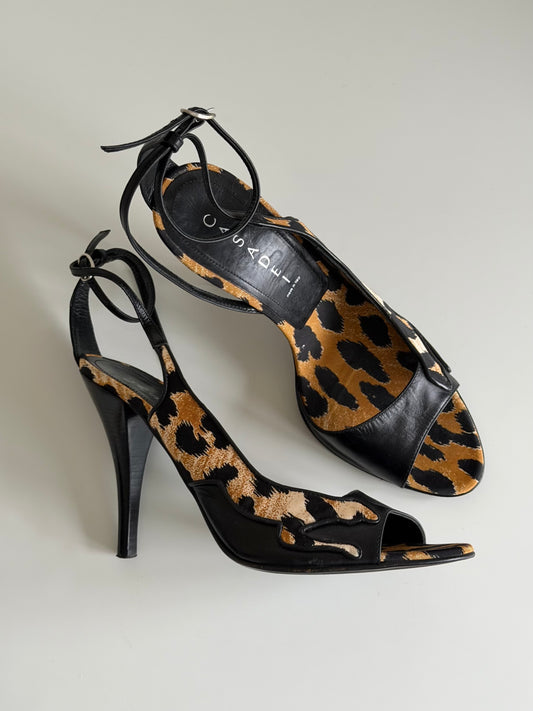 Black high-heeled shoes with leopard print insole on a light gray background
