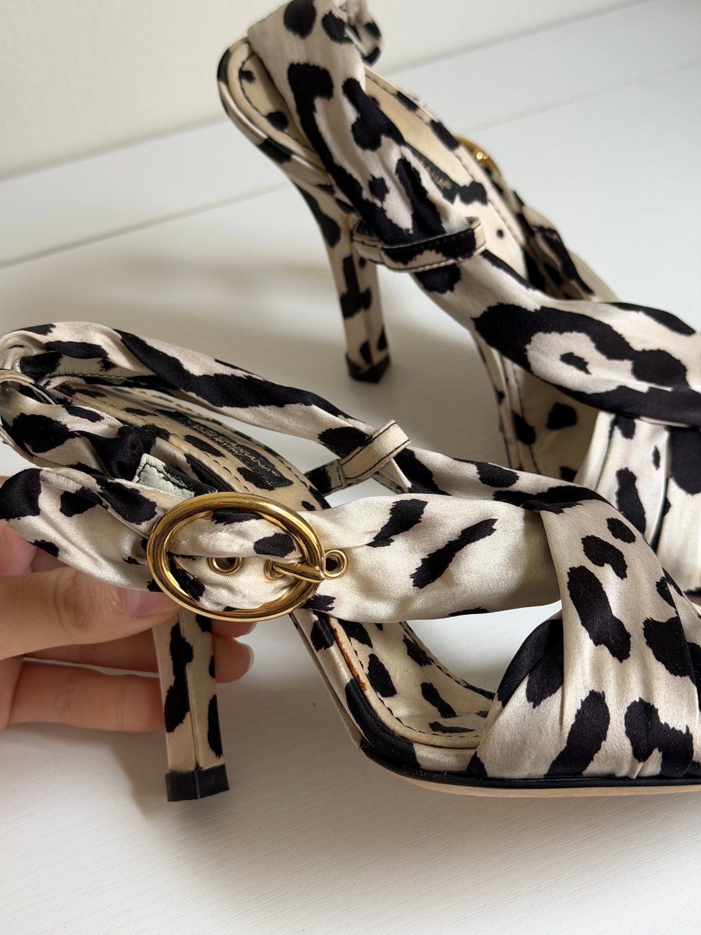 Leopard print handbag strap with gold ring detail held by a hand against a white background