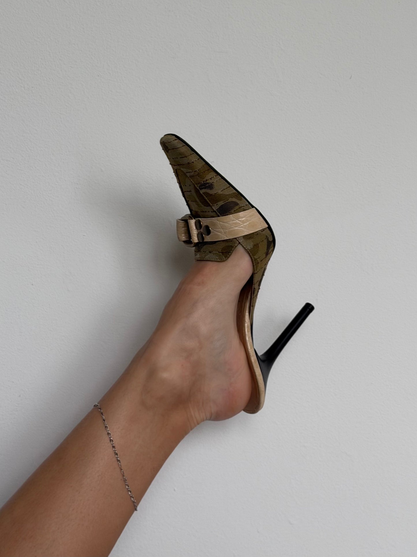 High-heeled shoe with a gold strap on a plain background