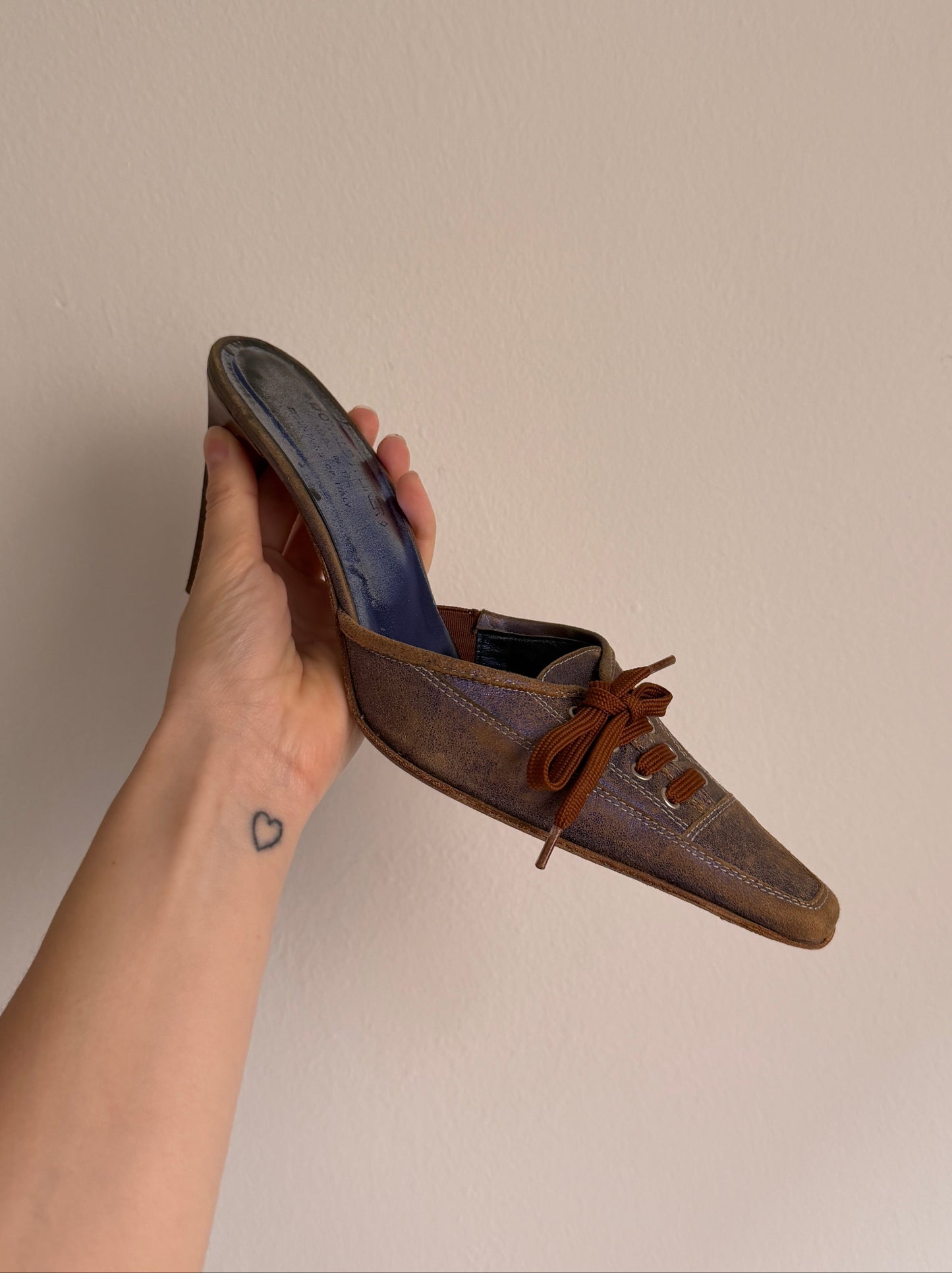 Brown shoe held by a hand against a plain background