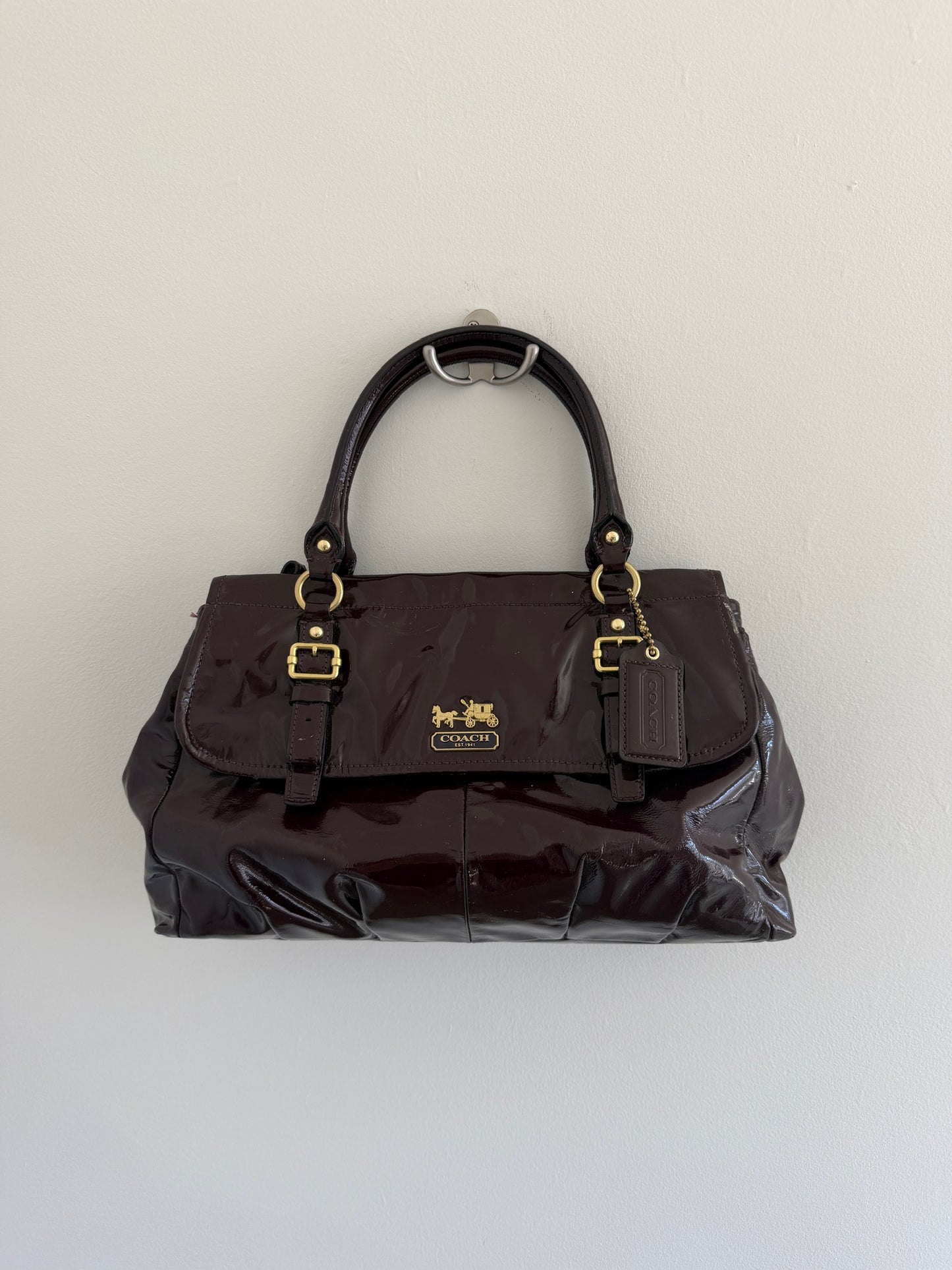 deep plum coach handbag with gold accents on a light gray background