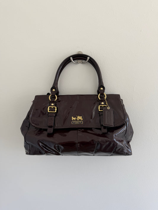 deep plum coach handbag with gold accents on a light gray background