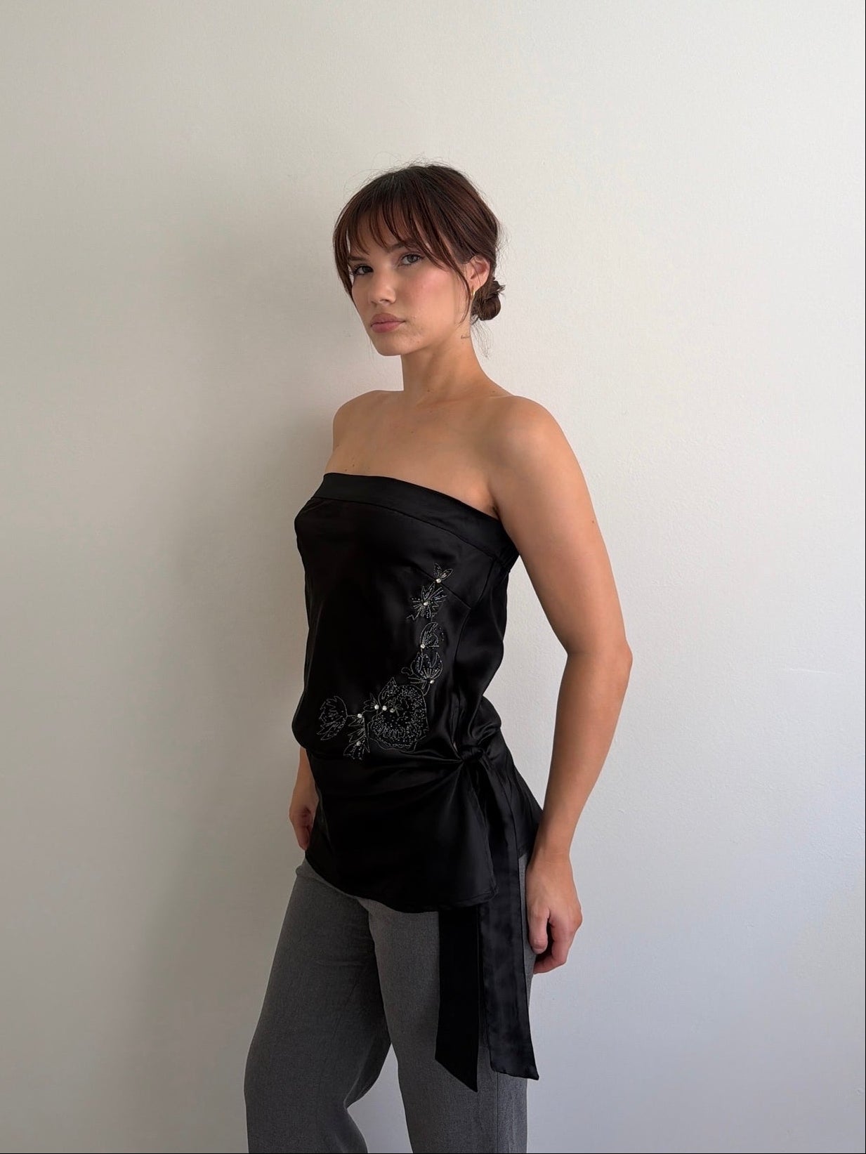Woman wearing a black strapless top with sequins against a plain background