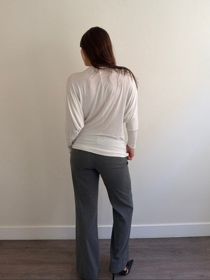 Person wearing a white top and gray pants standing against a plain wall.