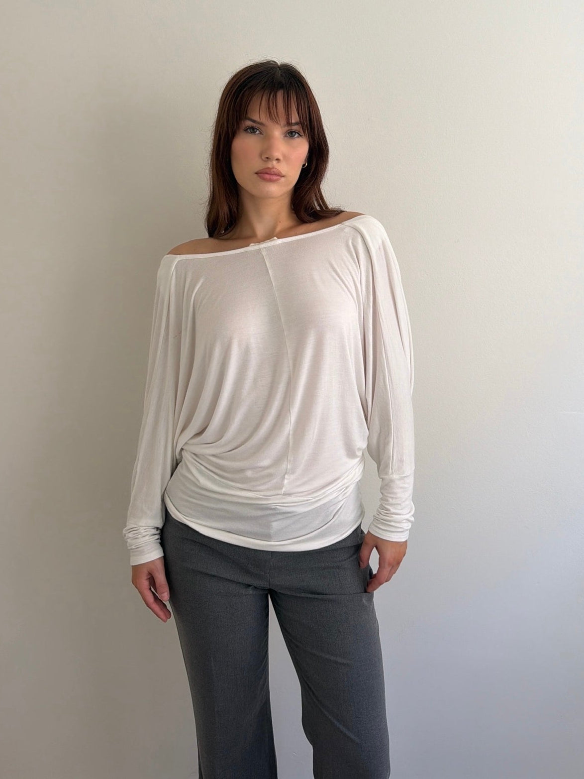Woman wearing a white off-shoulder top and gray pants against a plain background