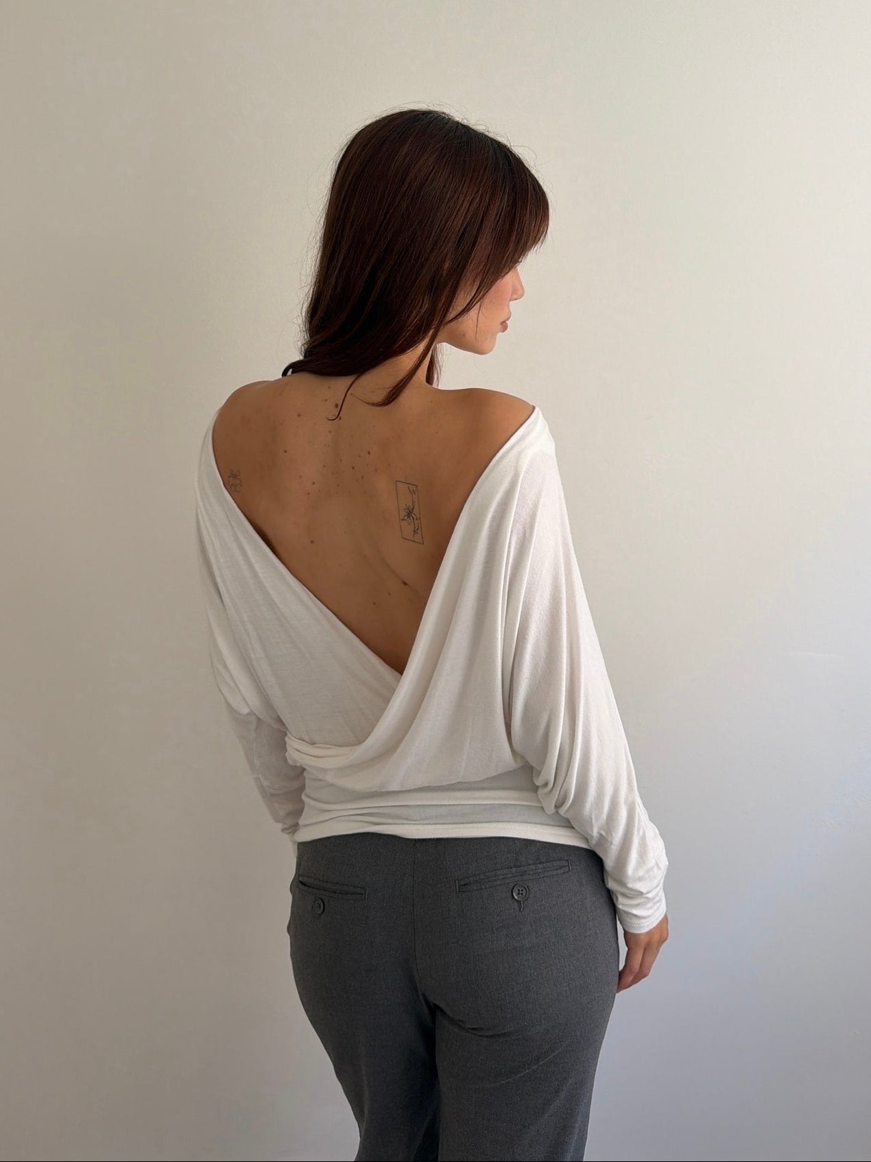 Person wearing a white off-shoulder top and gray pants against a plain background