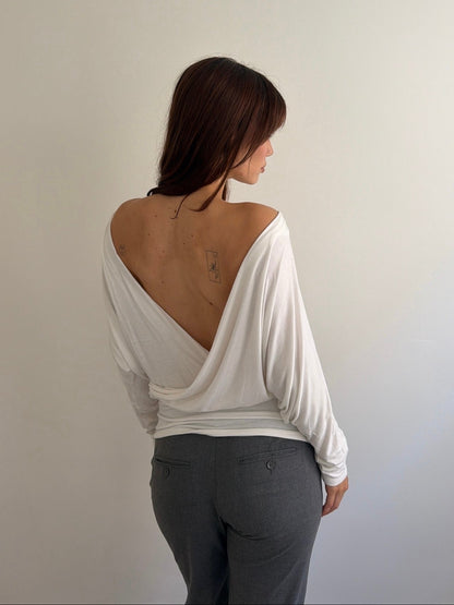 Person wearing a white off-shoulder top and gray pants against a plain background