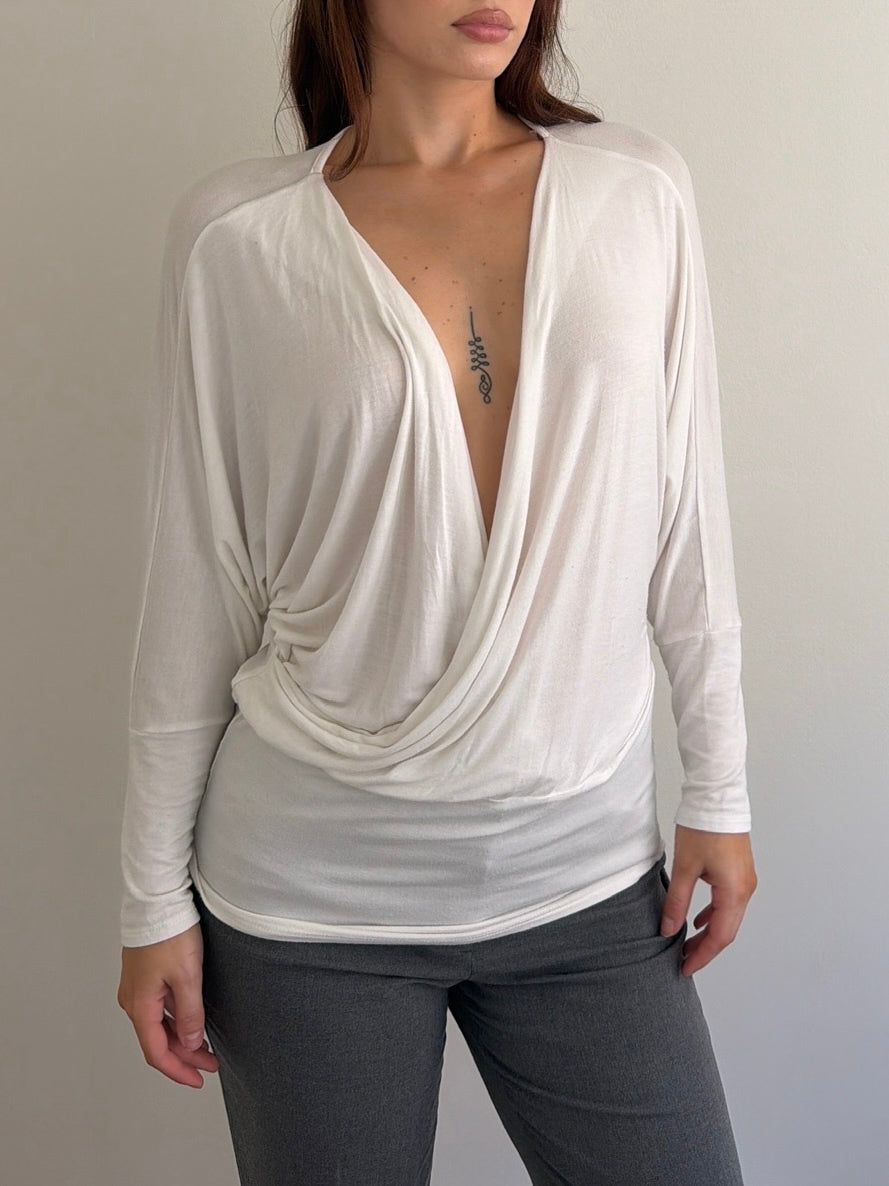 Woman wearing a white long-sleeve top with a deep neckline against a neutral background