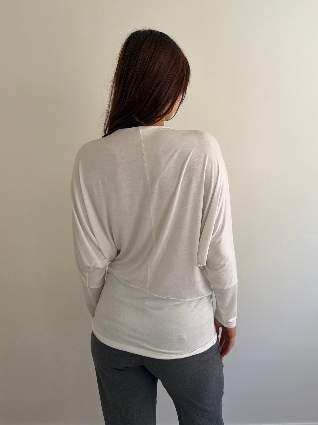 Person wearing a white long-sleeve top and gray pants against a plain background