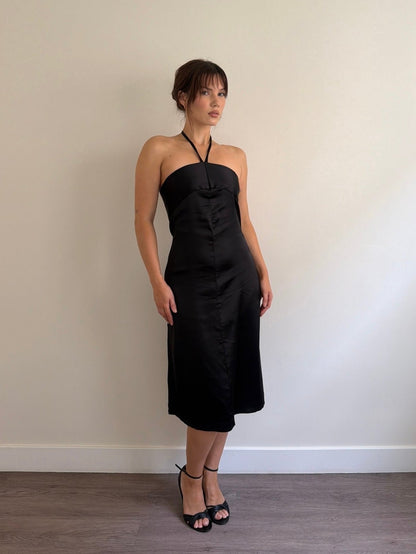 Woman wearing a black strapless dress against a plain wall.