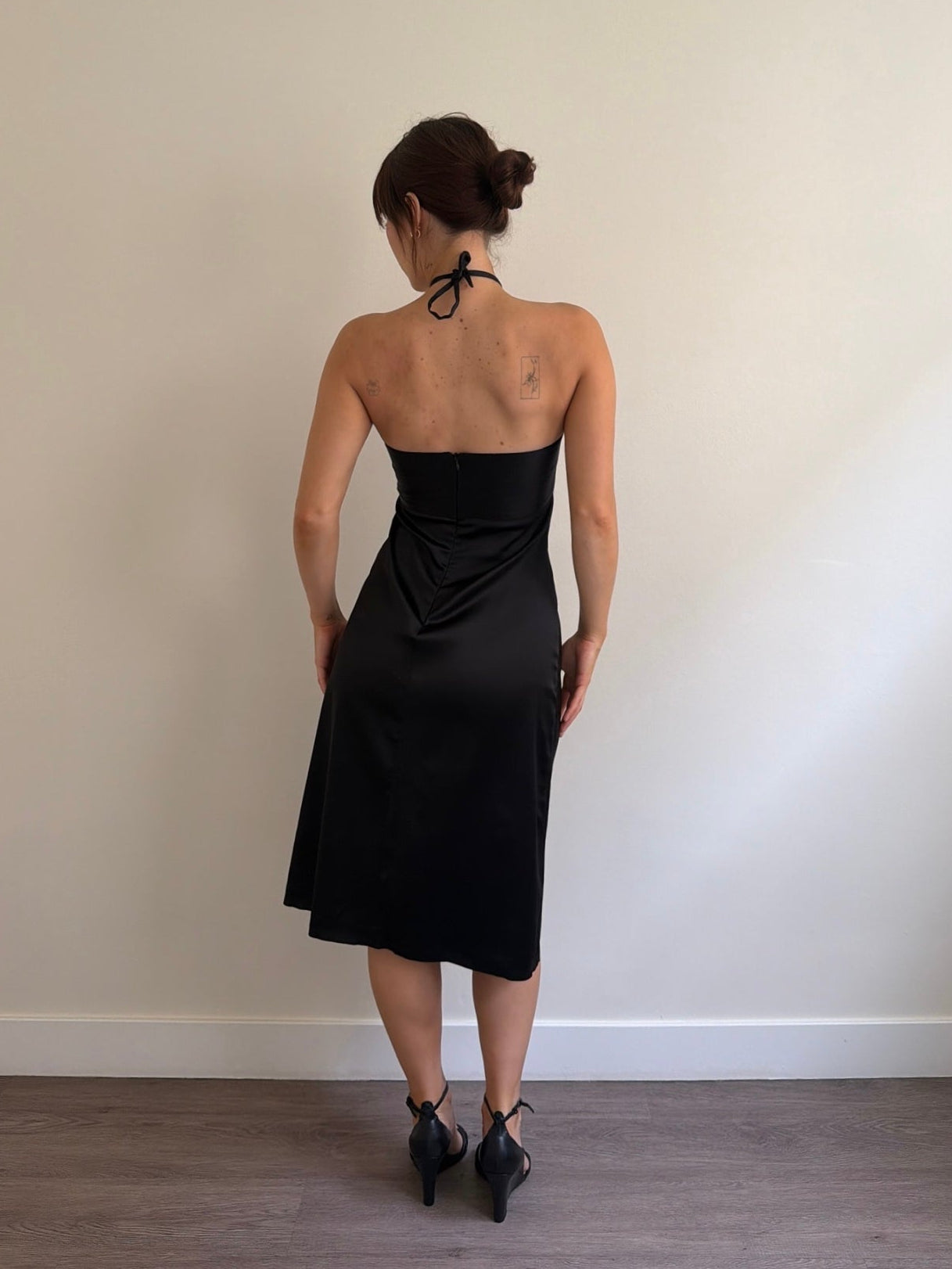 Woman wearing a black strapless dress against a plain wall.