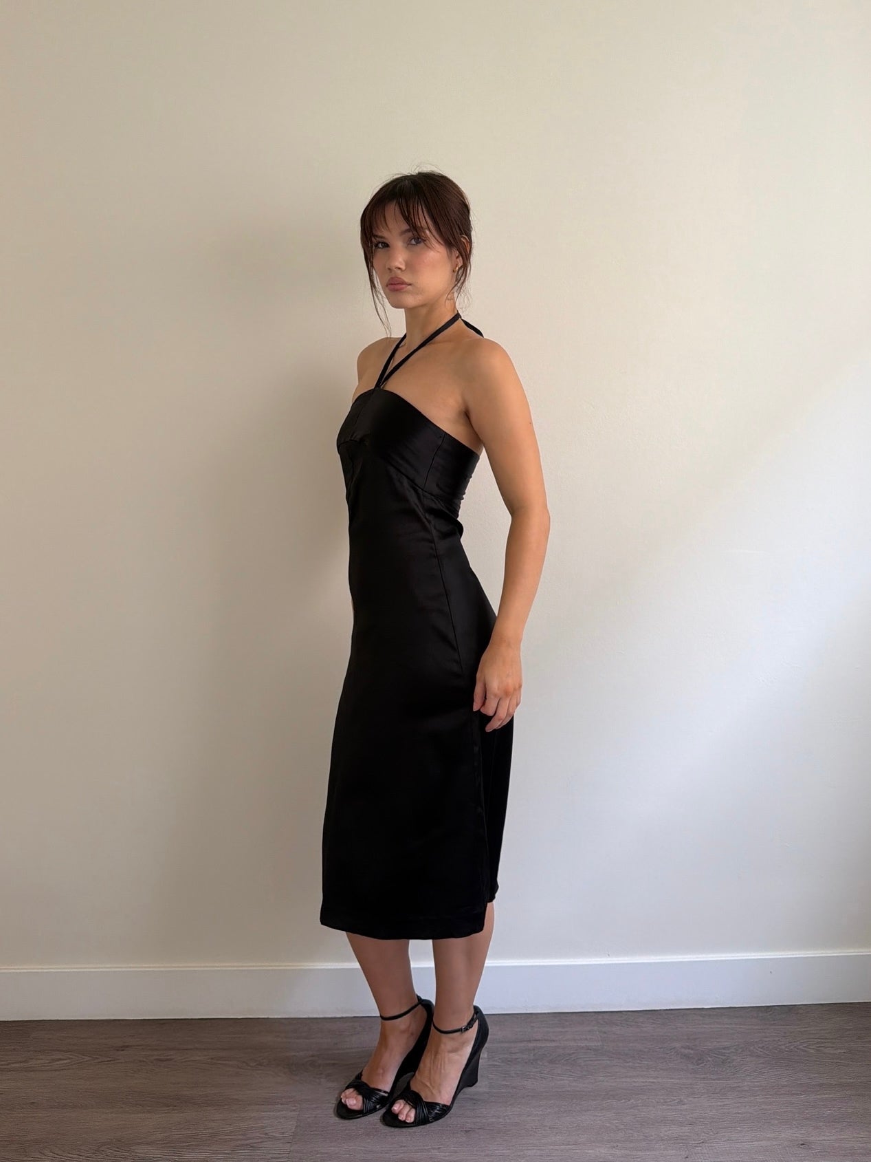 Woman wearing a black halter neck dress against a plain wall.