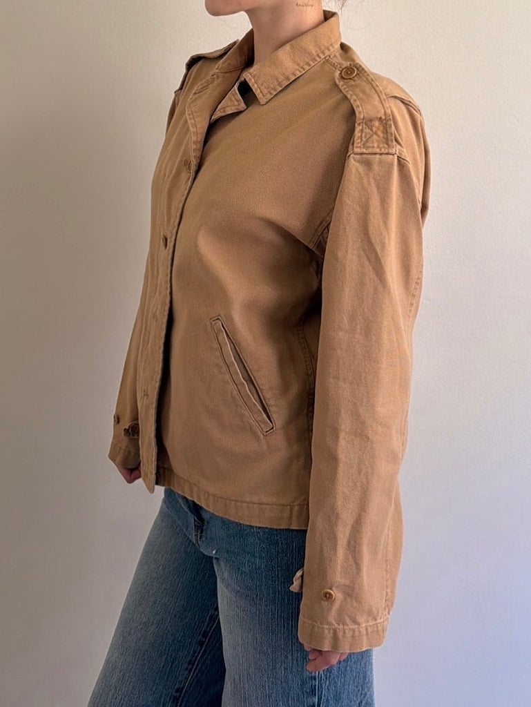 Person wearing a brown jacket and blue jeans against a plain background