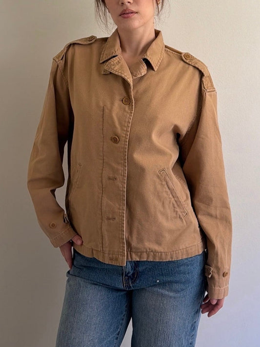 Person wearing a brown jacket and blue jeans against a plain background