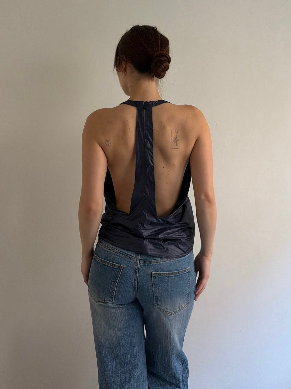 Person wearing a black halter top and blue jeans against a plain background