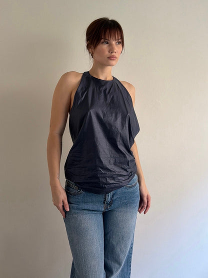 Woman wearing a dark gray sleeveless top and blue jeans against a plain background