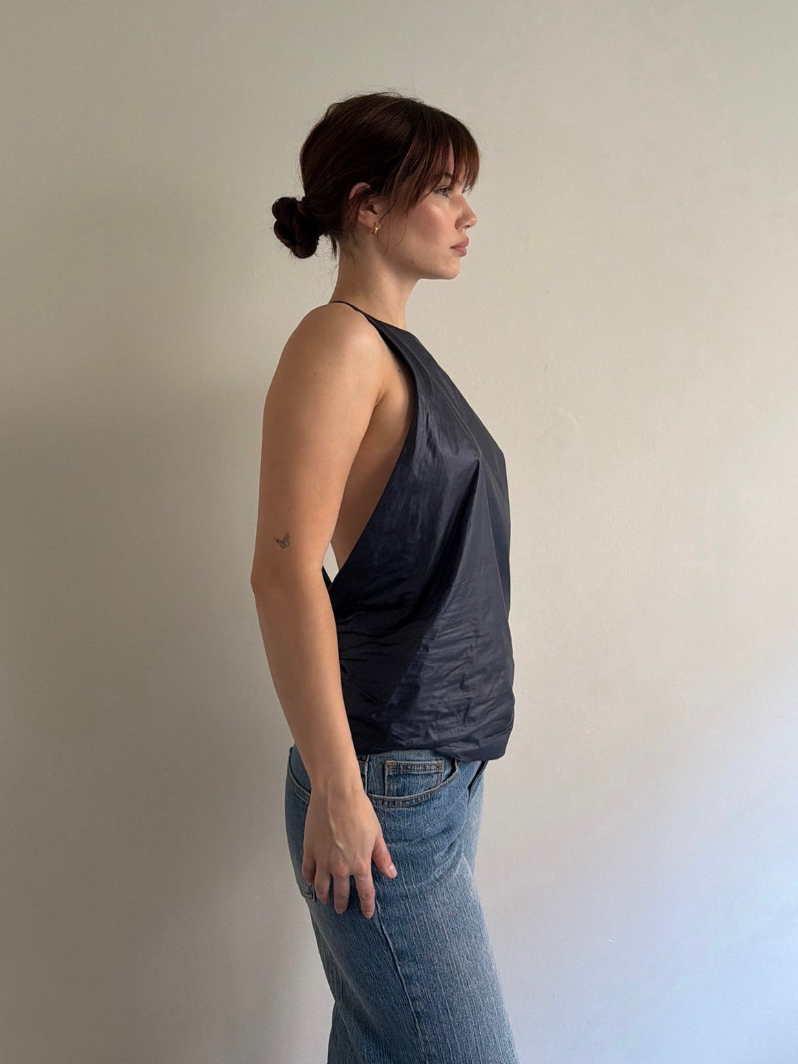 Woman wearing a dark gray tank top and blue jeans against a plain background
