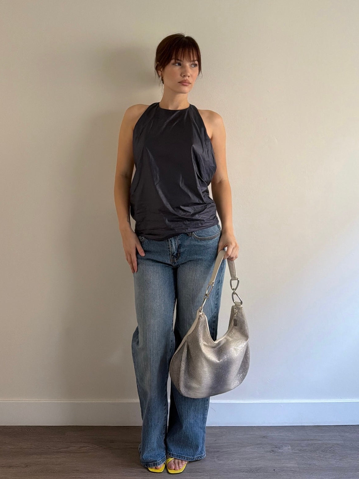 Woman holding a silver handbag against a plain wall