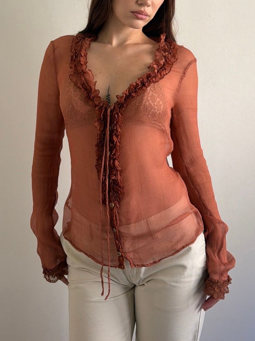 Woman wearing a rust-colored lace top against a plain background