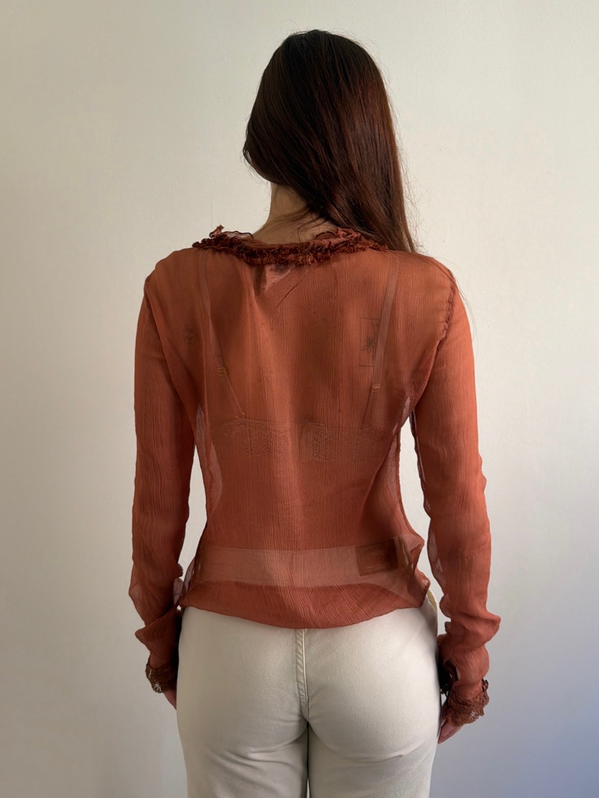 Person wearing a brown blouse with ruffled details on a plain background