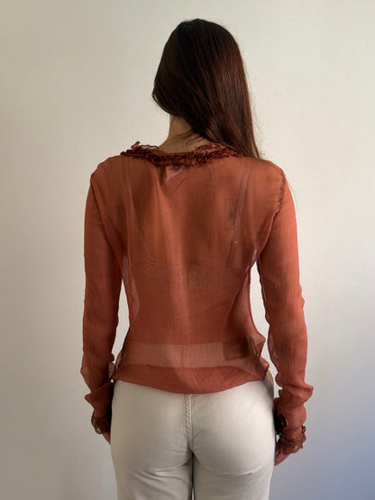 Person wearing a brown blouse with ruffled details on a plain background