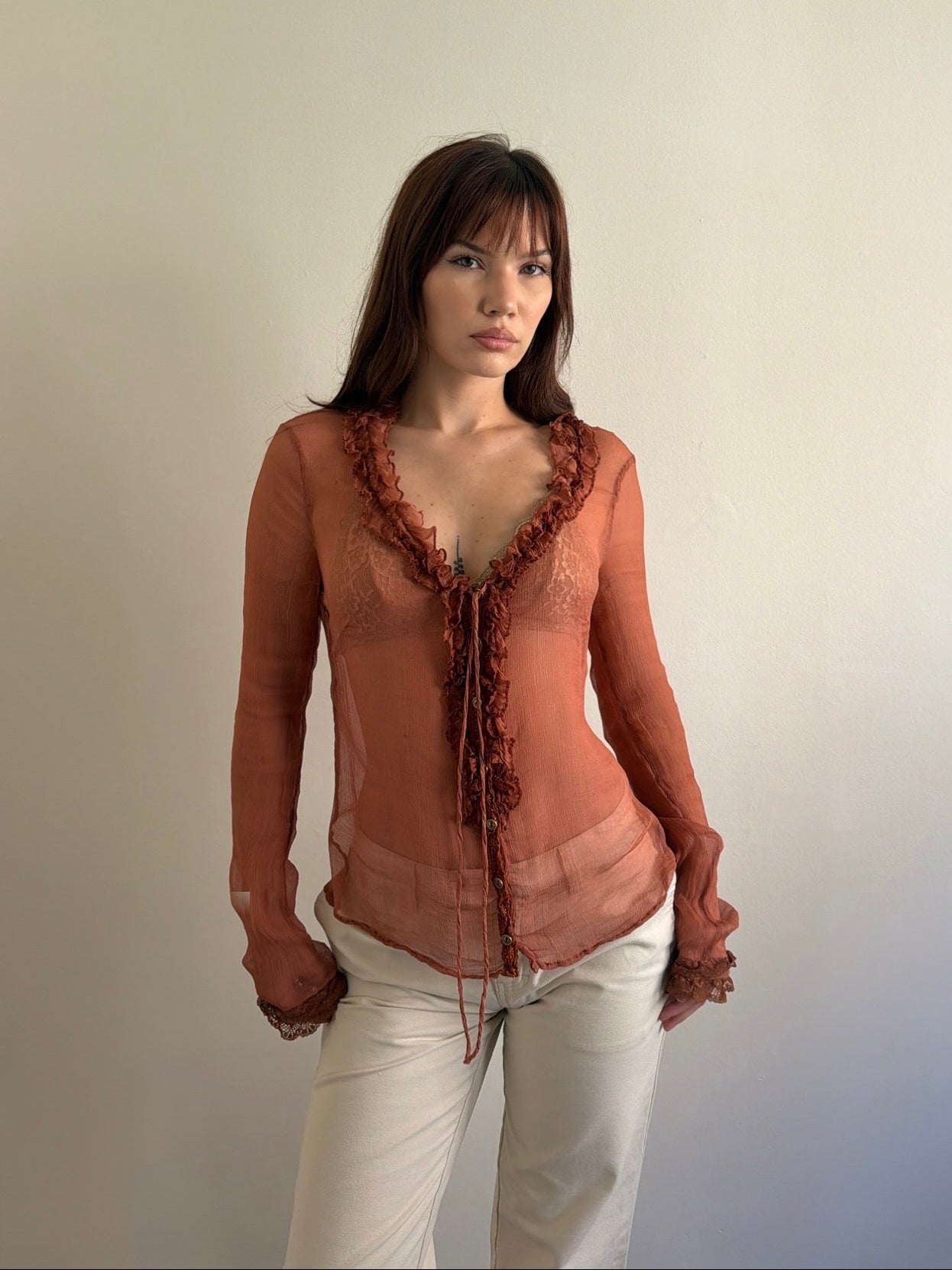 Woman wearing a sheer rust-colored top with lace details against a plain background