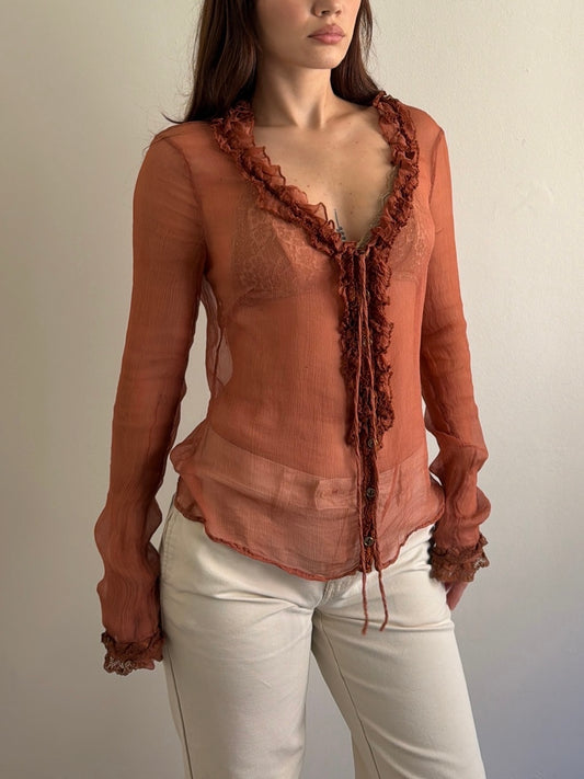Woman wearing a sheer rust-colored blouse with ruffled details on a plain background