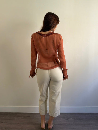 Person wearing a brown blouse and white pants standing against a plain wall.
