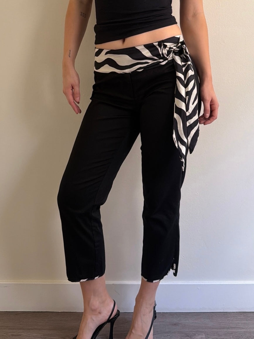 Person wearing black pants with a zebra-striped wrap over one shoulder against a plain background
