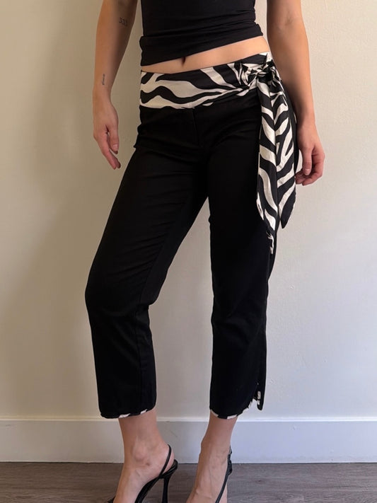 Person wearing black pants with a zebra-striped wrap over one shoulder against a plain background