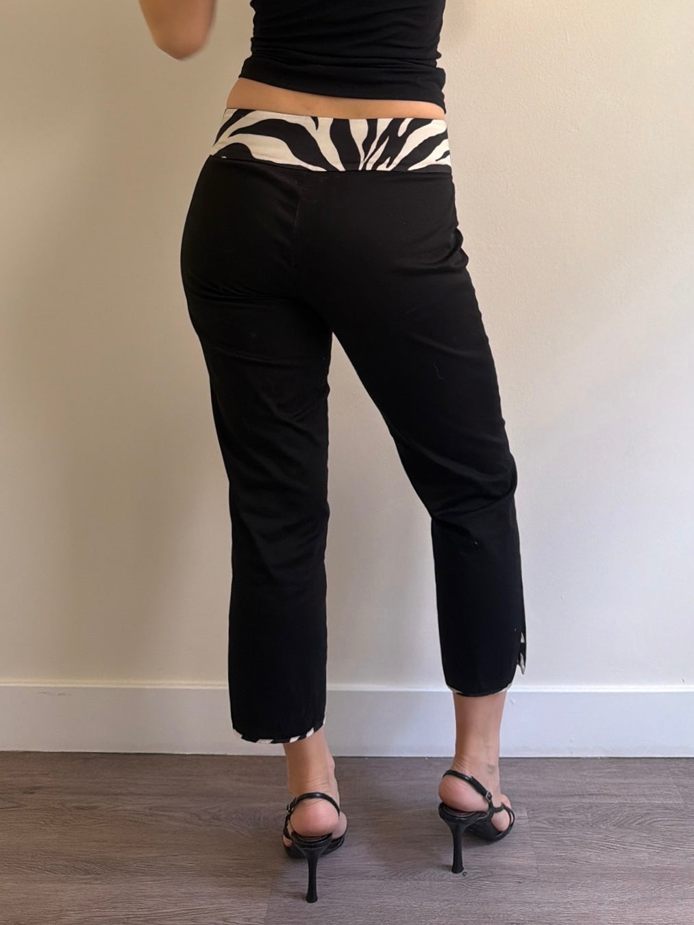 Person wearing black pants with zebra print waistband against a plain wall.