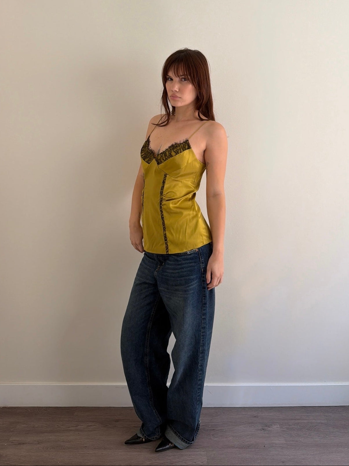 Woman wearing a yellow top and blue jeans against a plain wall.