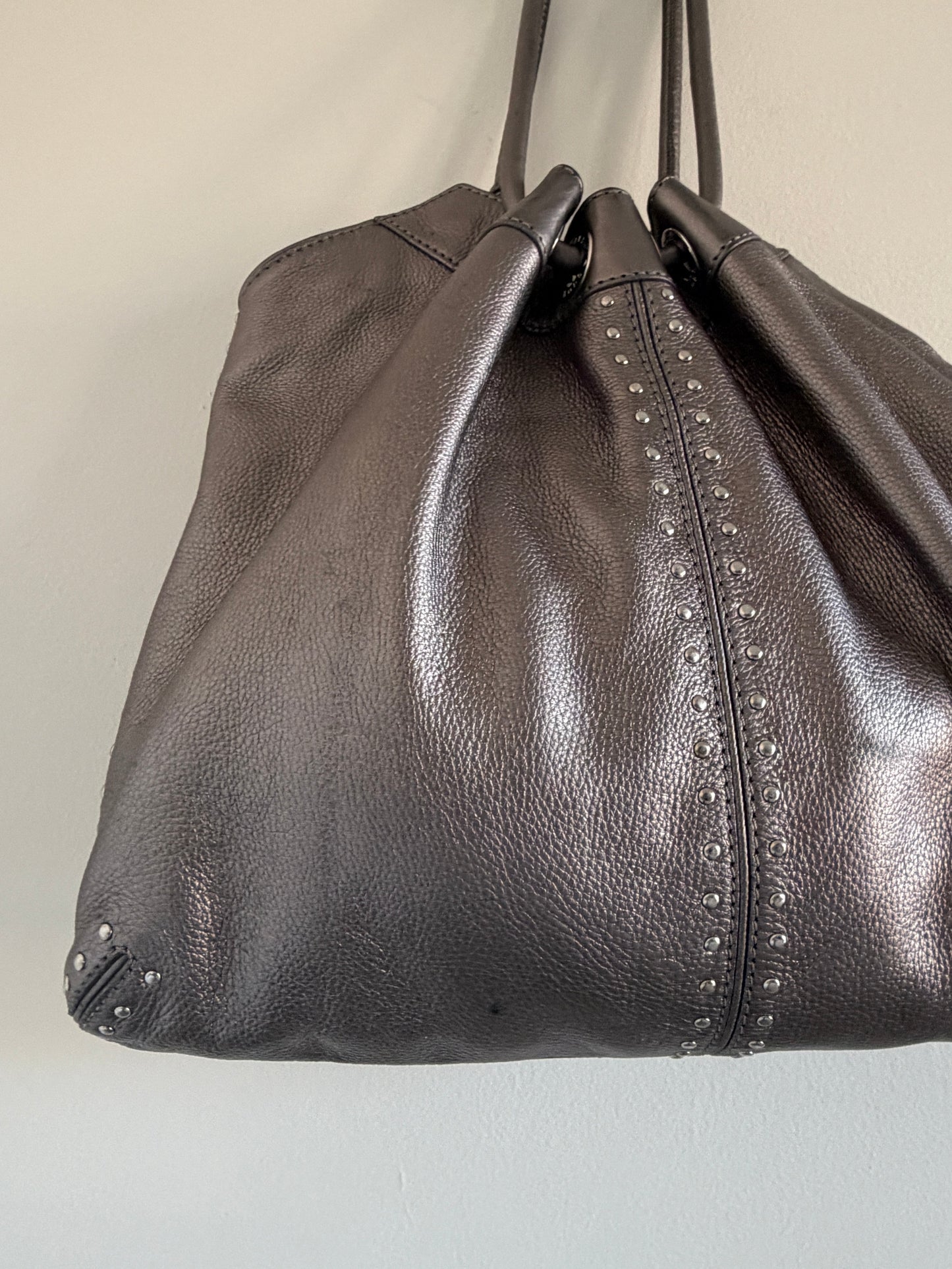 Close-up of a dark gray leather bag with studs on a light beige background