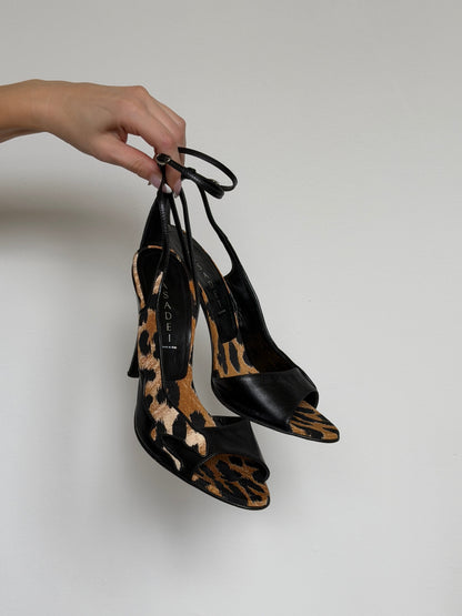 Pair of black and leopard print high-heeled shoes held by a hand against a plain background