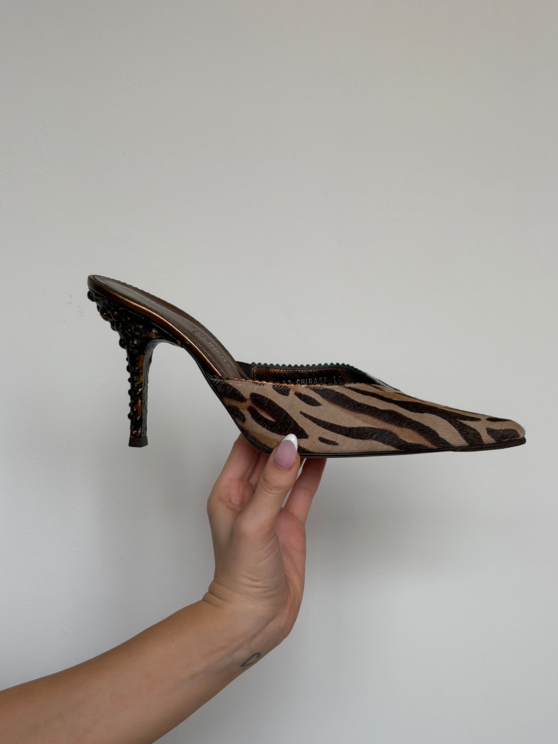 Hand holding a leopard print high-heeled shoe against a plain background