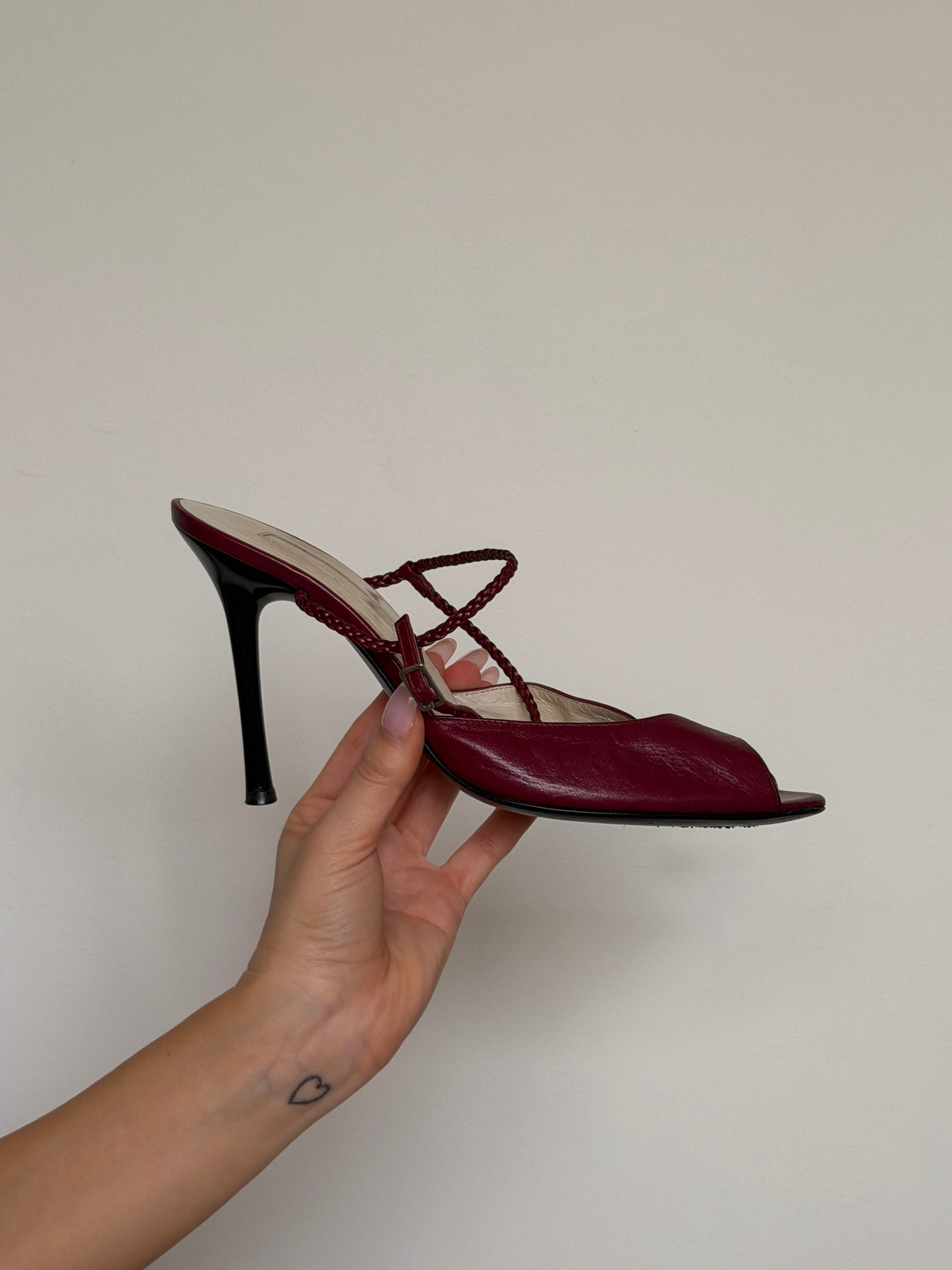 Red high-heeled shoe held by a hand against a plain background