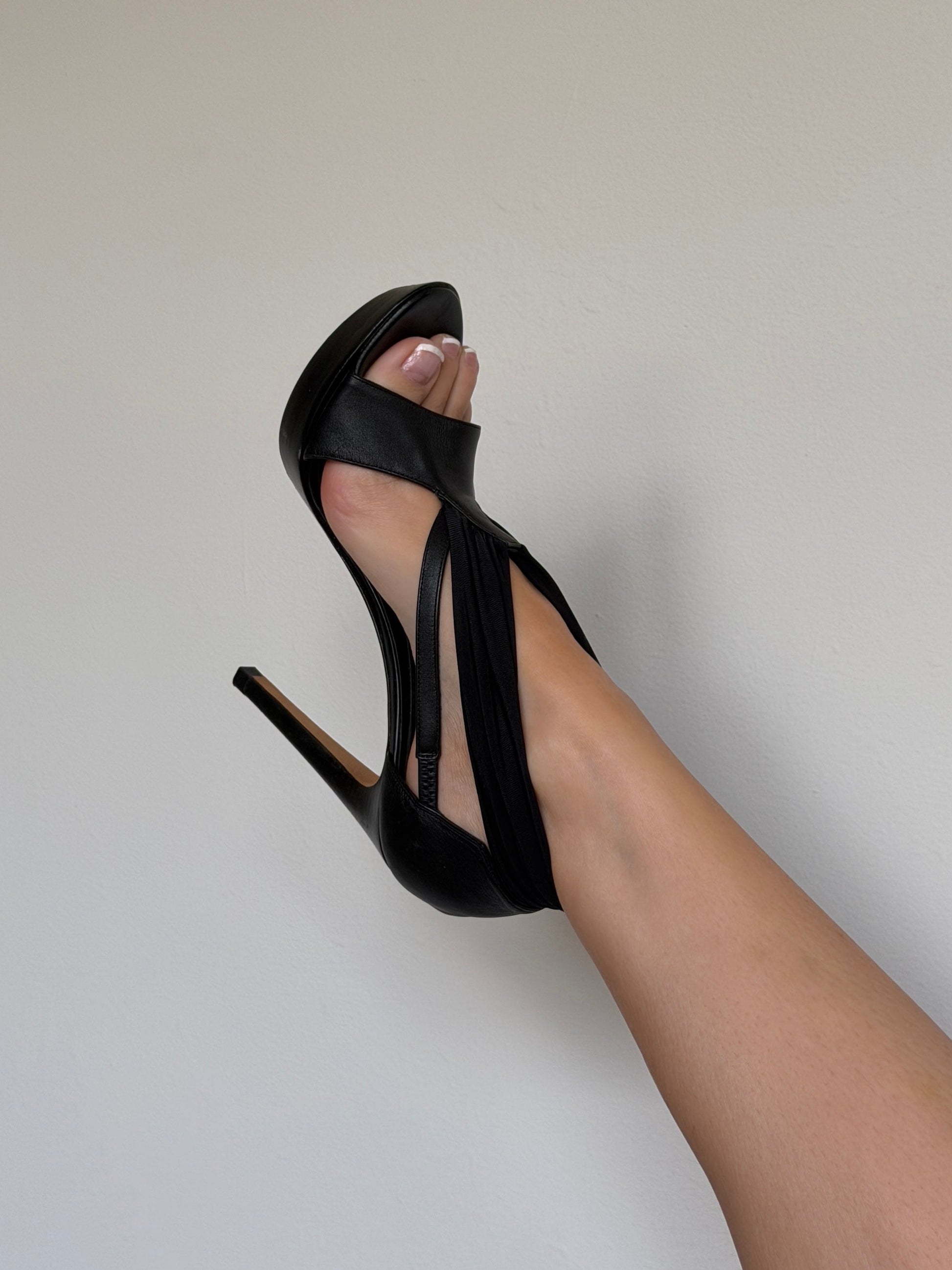 Black high-heeled sandals worn by a person on a plain background