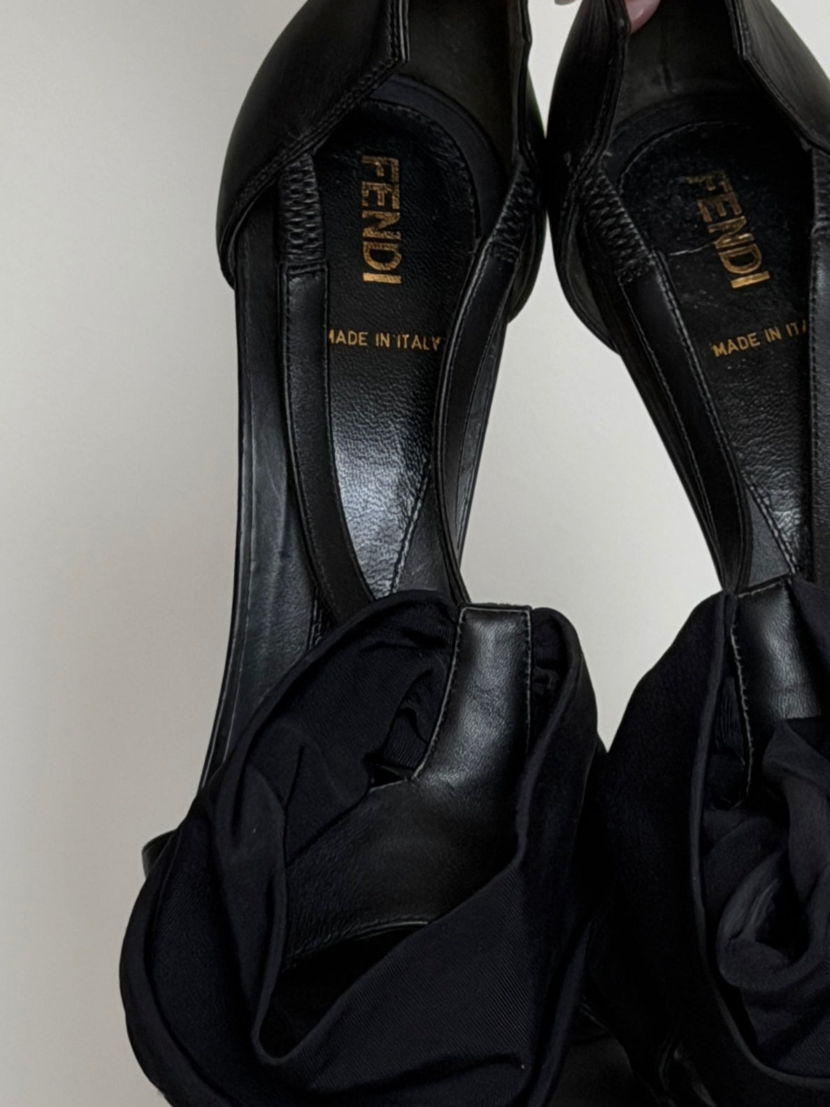 Black high-heeled shoes with 'Fendi' branding on a light gray background