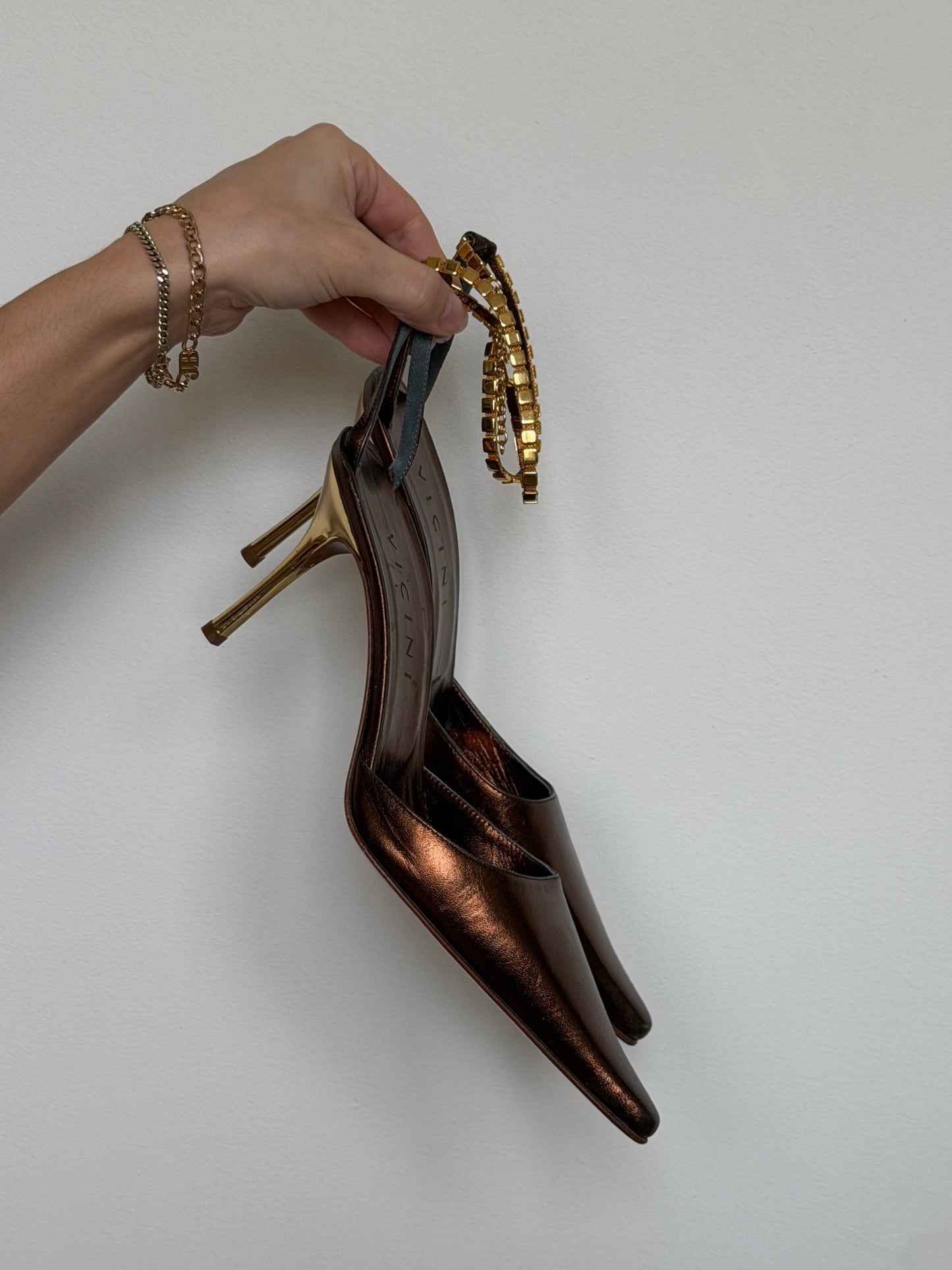 Brown high-heeled shoes with gold accents held by a hand against a white background