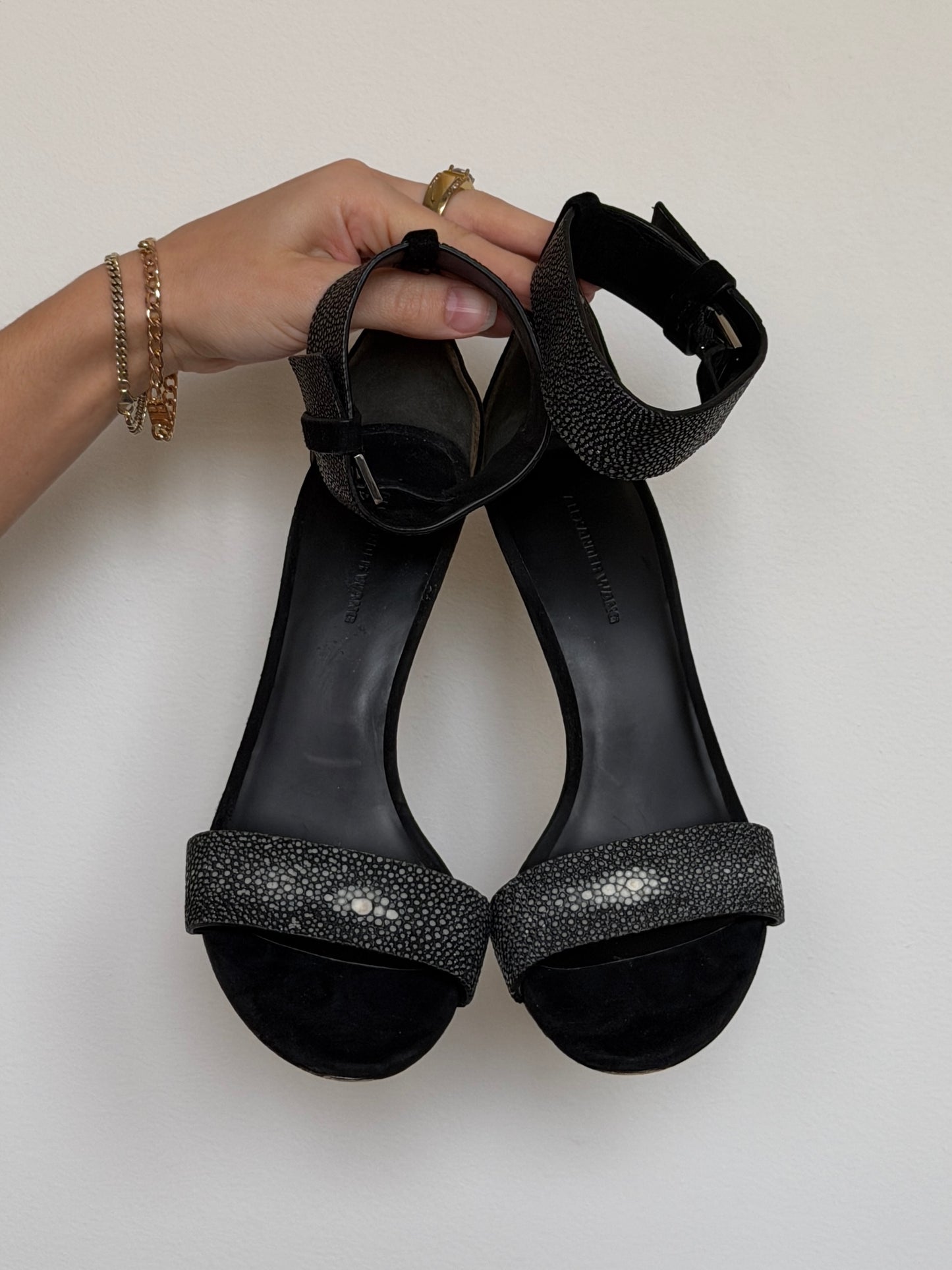 Black high-heeled sandals with glittery straps held by a hand on a light background