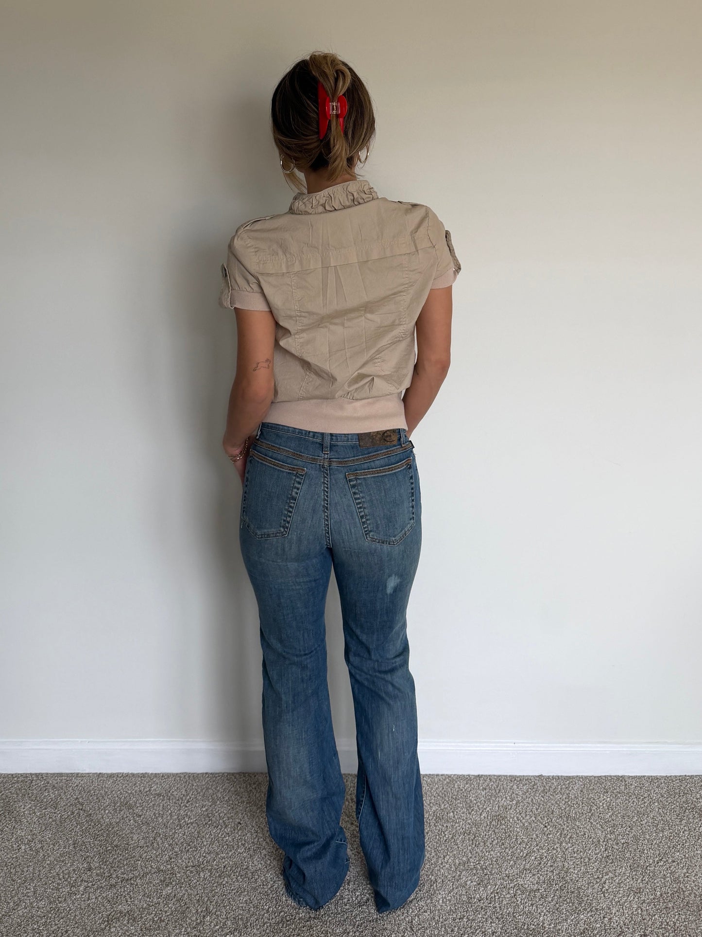 Person wearing a beige top and blue jeans standing against a plain white wall.
