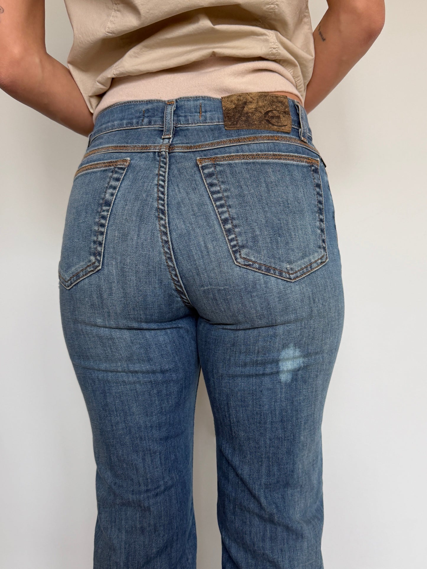 Person wearing blue jeans with a beige shirt against a plain background